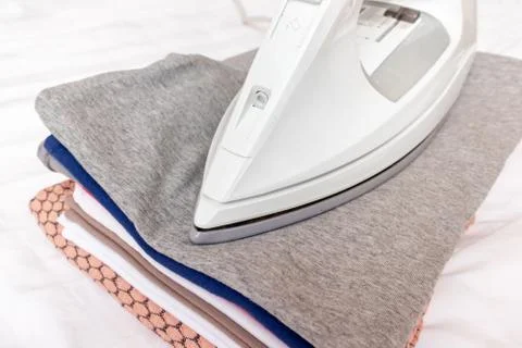 Modern electrical white iron on a stack of clothes close up - ironing, laundr Stock Photos