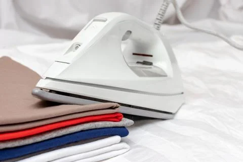 Modern electrical white iron on a stack of clothes close up - ironing, laundr Stock Photos