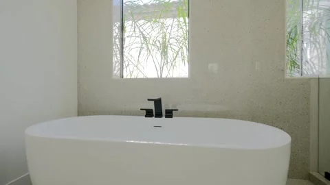 Modern elegant bathroom featuring white bathtub, black faucet and window with Stock Footage 274285767