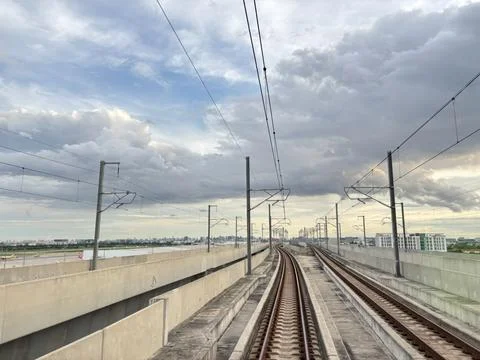 Modern elevated train tracks curving towards a cityscape under dramatic sky Stock Photos