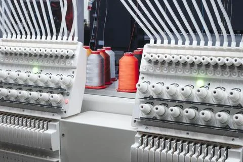 Modern embroidery machines with spools of thread. Bright orange and gray thre Stock Photos