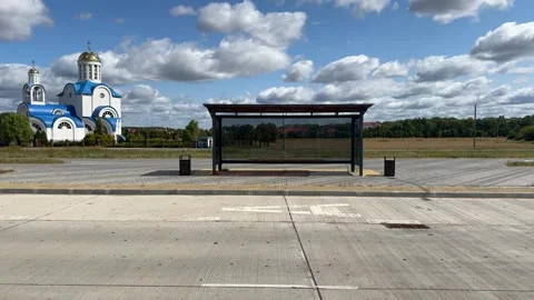 Modern empty bus stop shelter with glass panels near white orthodox church  Video stock 343407475