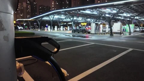 Modern EV charging station at night with bokeh city lights and moving vehicles. Stock Footage 330630693