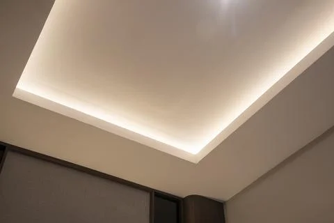 Modern false ceiling with warm recessed LED strip lighting above a paneled wa Stock Photos