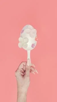 Modern flat lay Easter concept. A female hand holds a white egg on a stick. Stock Photos