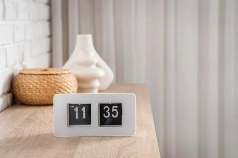 Modern flip clock displaying 11:35 AM on wooden table with home decor and whi Stock Photos