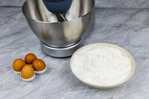 Modern food processor, eggs and plate with flour on a kitchen table Foto stock