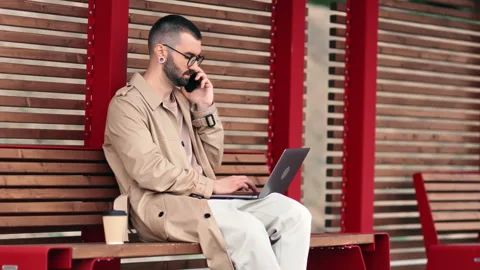 Modern freelancer business man working laptop talking smartphone waiting bus on Stock Footage 244081257