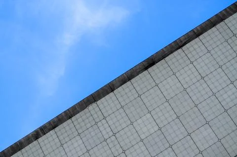 Modern geometric building facade under bright blue sky with wispy clouds. Stock Photos