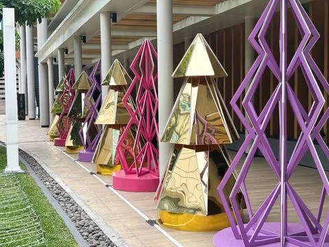 Modern, geometric Christmas tree installations lined up along an outdoor walkway Stock Photos