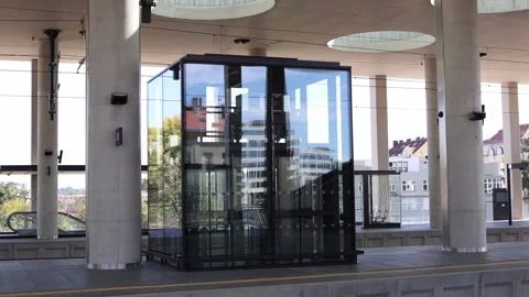 Modern glass elevator at a train station platform surrounded by tall concrete co Stock Footage 317506603