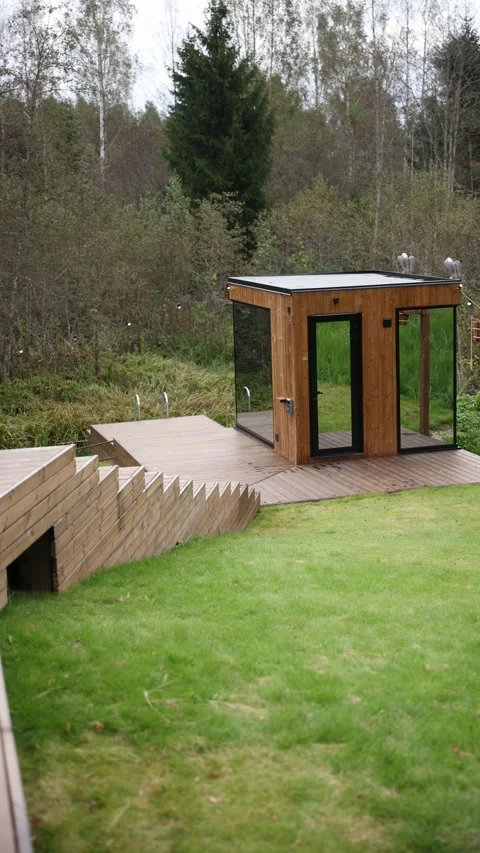 Modern glass sauna cube on deck by pond with birch and spruce Stock Footage 324795325
