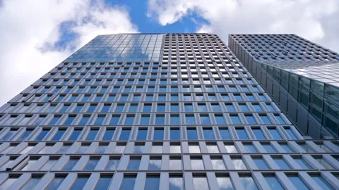 Modern glass skyscraper facade reflecting blue sky and clouds moving slowly.. 库存影片 339119398