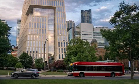 Modern glass skyscraper with sunset reflection and red city bus driving on .. Foto stock