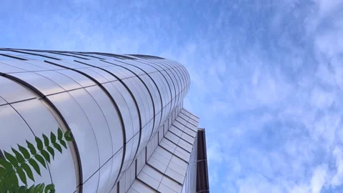 Modern glass skyscraper tower viewed from ground level against blue sky with Stock Footage 337104412