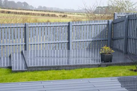 Modern gray deck meets green grass and wooden fence Stock Photos