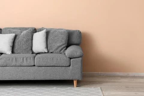 Modern gray fabric sofa with assorted cushions against a warm peach wall and  Stock Photos