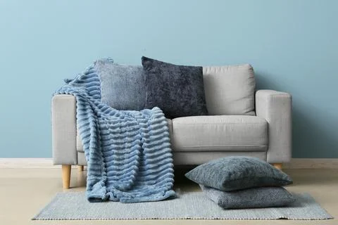 Modern gray sofa with blue textured blanket and decorative pillows against a  Stock Photos