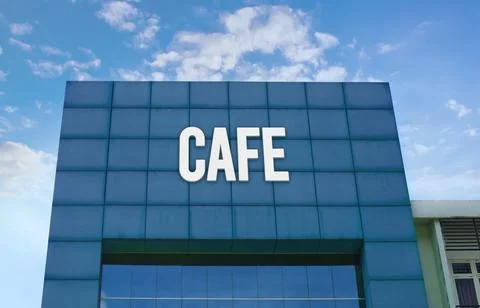 Modern green facade with a large CAFE sign against a cloudy blue sky. Stock Photos