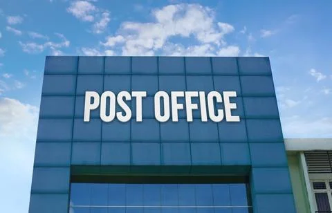 Modern green facade with a large POST OFFICE sign against a cloudy blue sky. Stock Photos