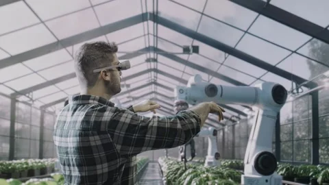 Modern Greenhouse Worker Using Augmented Reality Headset To Control Robotic Arms Stock Footage 293517476