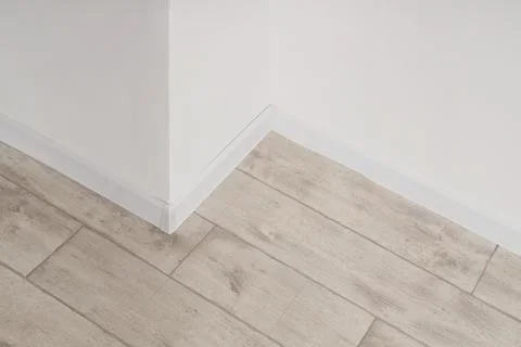 Modern home interior corner with light wood laminate flooring and white baseb Stock Photos