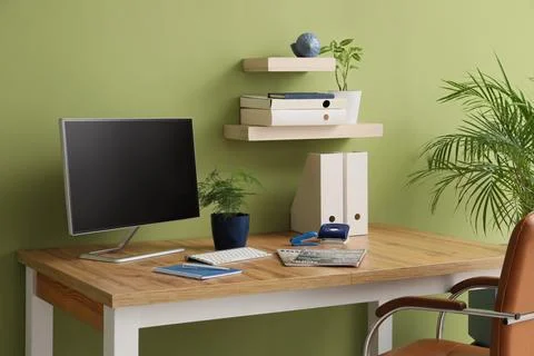 Modern home office workspace with computer monitor, wooden desk, and green wa Stock Photos