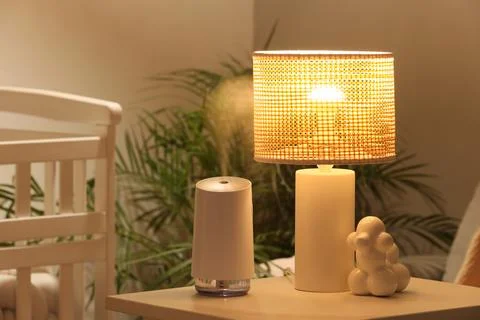 Modern humidifier and lamp on bedside table in children's bedroom at evening Stock Photos
