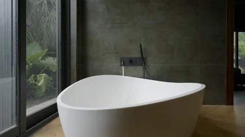 Modern interior design of bathroom with large ceramic bathtub in middle, dark Stock Footage 259715173