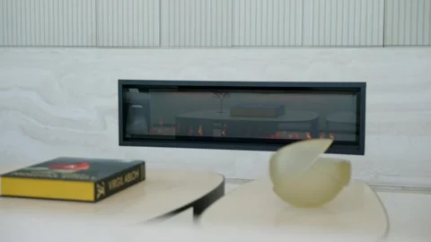 Modern interior space featuring sleek, rectangular fireplace embedded in light Stock Footage 295551154
