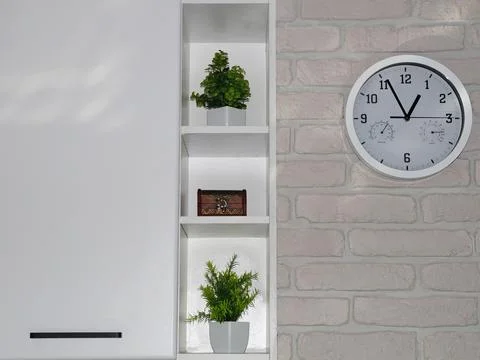A modern interior with a wall clock and green plants on white shelves against Stock Photos