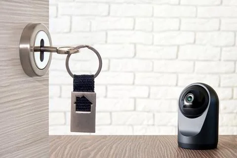 Modern IP camera on the table and opened house door with key inside Stock Photos