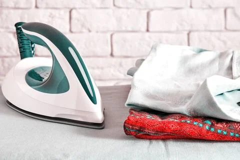 Modern iron on the ironing board with stack of ironed clothes Stock Photos