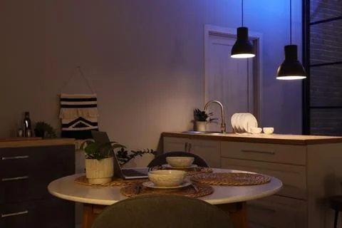 Modern kitchen and dining area with warm and cool lighting, laptop on table,  Stock Photos
