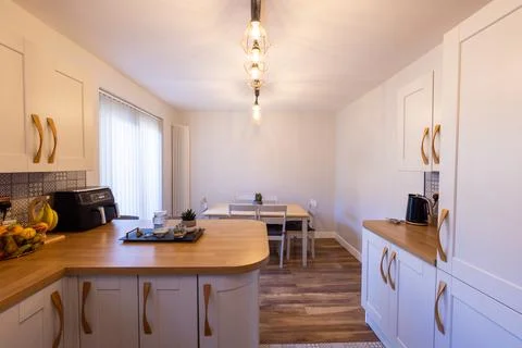 Modern kitchen and dining area with white fitted cabinets wooden worktops b.. 库存照片