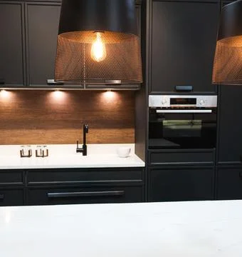 Modern kitchen interior featuring dark cabinets, white countertop, wood bac.. Stock Photos