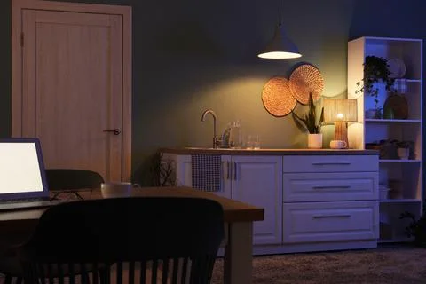 Modern kitchen interior at night with warm lighting, laptop on dining table,  Stock Photos