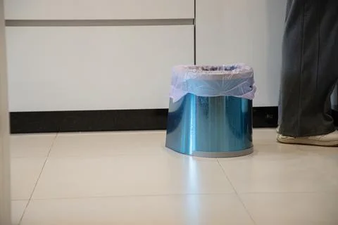 In a modern kitchen, a small trash bin stands near a person about to discard Stock Photos