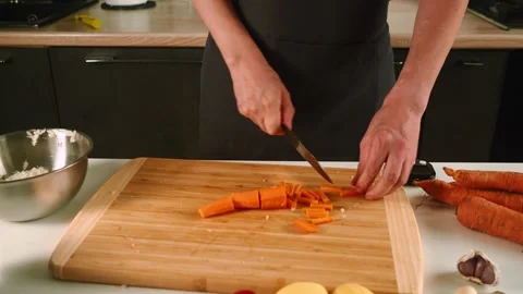 In a modern kitchen, someone skillfully chops bright orange carrots on a wooden Stock-Footage 316633866