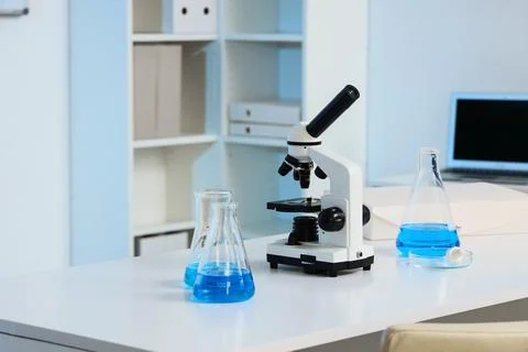 Modern laboratory microscope and blue liquid in erlenmeyer flasks on a white  Stock Photos