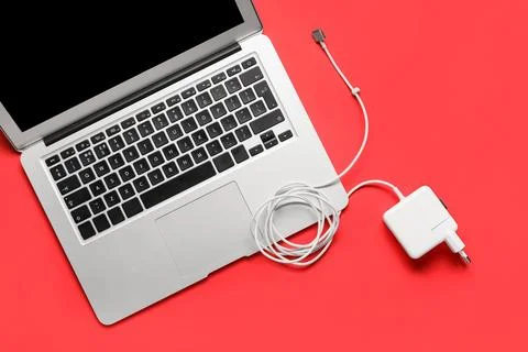 Modern laptop computer with power adapter and charging cable on a bright red  Stock Photos