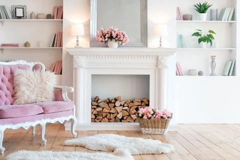 Modern light interior with fireplace, spring flowers and cozy pink sofa Stock Photos
