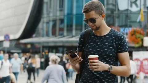 Modern man with a cup of coffee use mobile phone on crowded city street Stock Footage 116659193