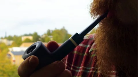 Modern man with long ginger beard is smoking his lovely black pipe with Stock Footage 253139321
