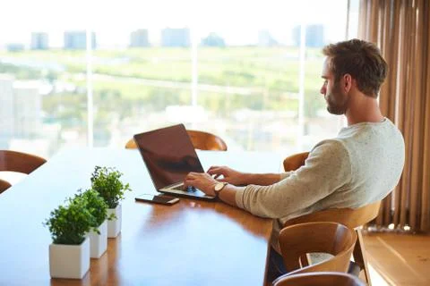 Modern man sitting at dining table with his laptop working Fotos Stock