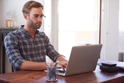 Modern man typing on a laptop while seated at desk Stock Photos