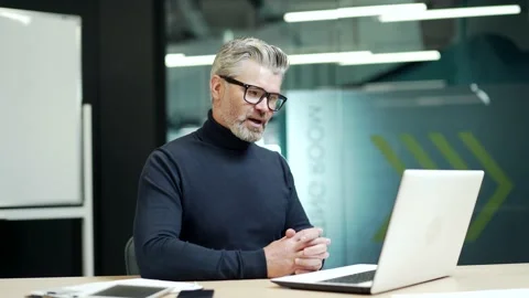 Modern mature gray haired bearded man is making a video call using a laptop whil Stock Footage 232581022