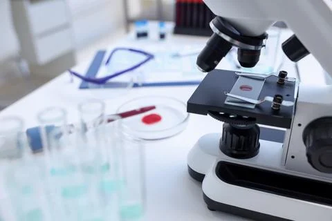 Modern medical microscope with sample of red liquid on white table in labor.. Stock Photos