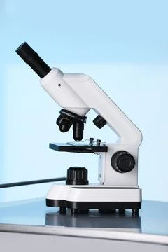 Modern microscope on metal table against light blue background Stock Photos