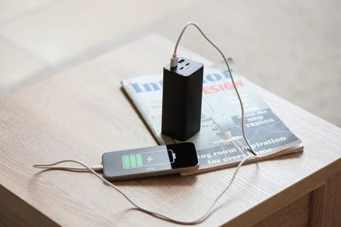 Modern mobile phone with charging cable, power bank and magazine on table in  Stock Photos